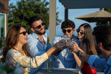 Young people having fun, outdoor party on sunset, group of friends smiling and laughing, drinking champagne for celebration toast