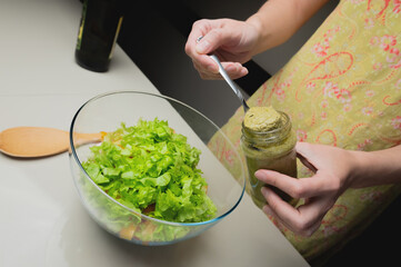 Pouring delicious sauce from a jar over fresh vegetables in a glass bowl. Young wife cooks healthy food