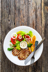 Barbecued pork chops with fried potatoes and fresh vegetables on wooden table
