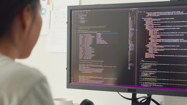 Close-up young Asia girl IT development programmer typing on keyboard coding programming fixing database code on computer monitor and laptop screen on table in workroom at house office.