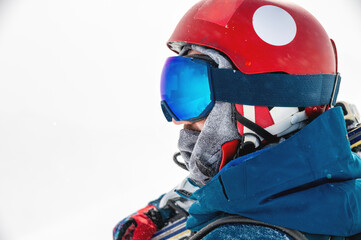 Naklejka premium sportsman in a helmet and goggles in profile against the background of white falling snow, looks to the side enjoying a beautiful view of the mountains