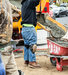 Wet cement off loaded by construction workers using a shovel from a cement truck chute into a wheelbarrow