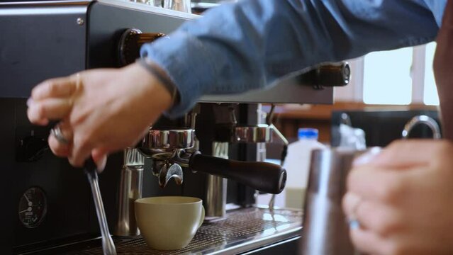 Closeup hands of barista preparing steam milk or foam for making coffee in pitcher in coffee shop, close-up young asian woman making cappuccino or latte with machine, small business or SME.