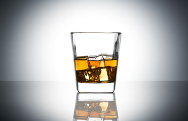 Crystal classic glass of whiskey with ice cubes on grey gradient background. Glass of scotch whiskey and ice on grey gradient background. Glass of whiskey on a glossy surface