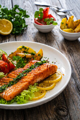 Seared salmon steak with fried potatoes and fresh vegetable salad served on wooden table
