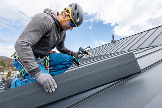 A roofer with a safety harness and tool belt is working with a