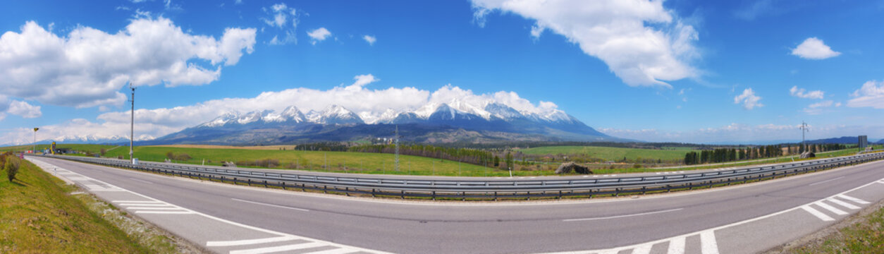 highway through the slovakian countryside, revealing a scenic view of the beautiful tatra mountains. the road leads through vast farmland, providing a beautiful backdrop for the journey