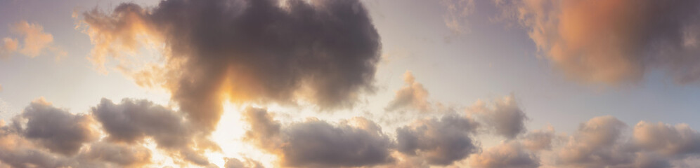 panorama of a sky in warm evening light. massive clouds in orange color at sunset