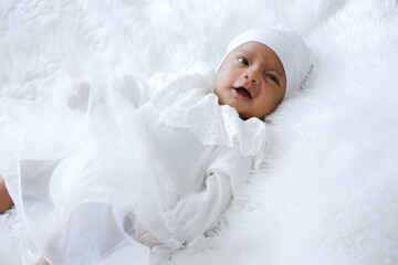 Portrait of newborn laughing while lay down on white bed in white dress.