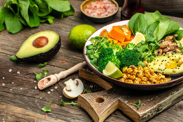 healthy vegan lunch bowl with Avocado, mushrooms, broccoli, spinach, chickpeas, pumpkin on a wooden background. vegetables salad. Top view