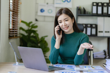 Smiling asian businesswoman working at home office talking on mobile and laptop with financial graph, accounting concept