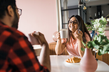 Young diverse loving couple eating croissant and talks together at home in breakfast time. Communication and relationship concept