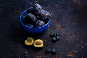 Ripe juicy plums and blueberries in a bowl on a table. Summer fruits.