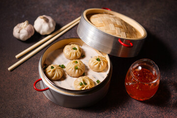 Traditional dumplings in bamboo steamer with sauces and chopsticks on dark, wooden surface with copy space, food background, dumpling steamer basket, gyoza, dimsum,  menu, oriental, fine dining
