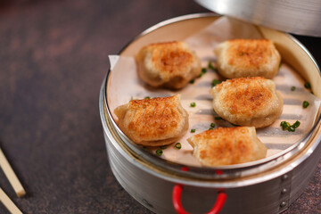 Traditional dumplings in bamboo steamer with sauces and chopsticks on dark, wooden surface with copy space, food background, dumpling steamer basket, gyoza, dimsum,  menu, oriental, fine dining