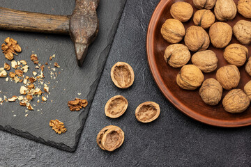 Crushed walnuts and rusty old hammer on stone board. Nut shell on the table. Whole nuts on ceramic plate.