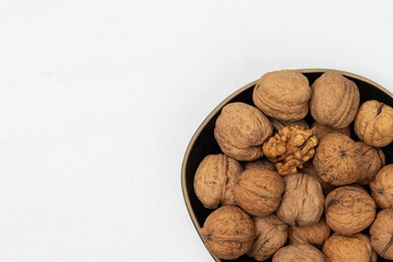 Walnut kernel and whole nuts in a black bowl.