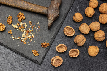 Crushed walnuts and a rusty old hammer on a stone board. Nut shell and whole nuts on the table.