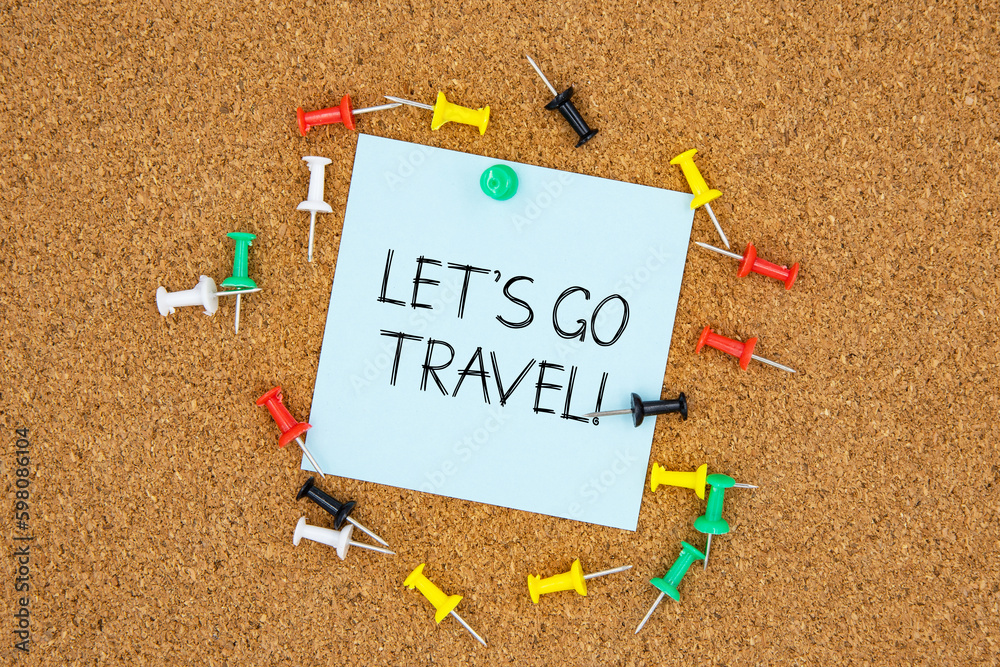 Fototapete let's go travel text on light blue post-it paper pinned on bulletin cork board surrounding by multi 