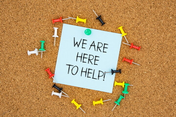 We are here to help text on light blue post-it paper pinned on bulletin cork board surrounding by multi color pins. This message can be used in business concept about offering help.