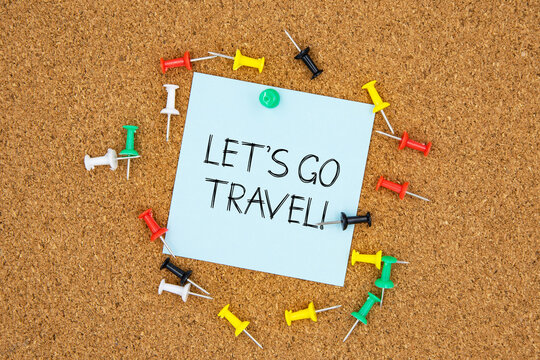 Let's go travel text on light blue post-it paper pinned on bulletin cork board surrounding by multi color pins. This message can be used in business concept about travel.