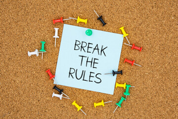 Break the rules text on light blue post-it paper pinned on bulletin cork board surrounding by multi color pins. This message can be used in business concept about breaking the rules.