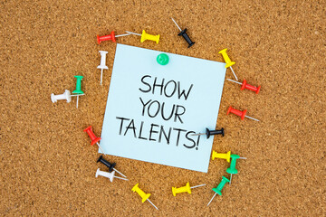 Show your talents text on light blue post-it paper pinned on bulletin cork board surrounding by multi color pins. This message can be used in business concept about talents.