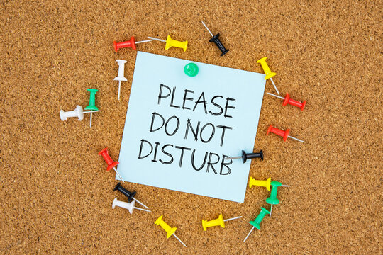 Please do not disturb text on light blue post-it paper pinned on bulletin cork board surrounding by multi color pins. This message can be used in business concept about asking to do not disturb.