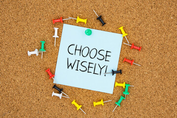 Choose wisely text on light blue post-it paper pinned on bulletin cork board surrounding by multi...