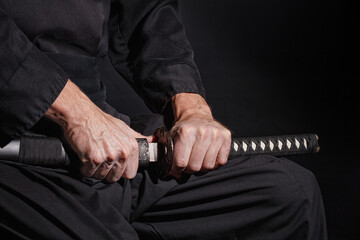 The samurai holding a Japanese katana sword. Photo of a warrior dressed in black clothes in low key with selective focus