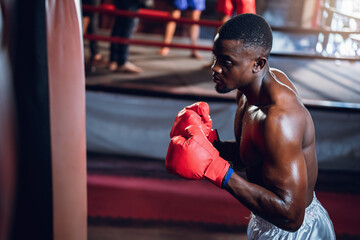 Boxing training of athlete african american man punching a bag at muay thai gym. Active male workout sport club for cardio and body strength. Health and lifestyles concept. - obrazy, fototapety, plakaty