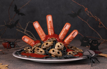 Themed food for Halloween - bloody hand from sausages with ketchup, mushrooms in form of skulls and black spaghetti - obrazy, fototapety, plakaty
