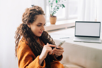 Happy Young Woman Using Smartphone for Remote Work or E-Learning from Home Office. Happy woman using cellphone for remote work and learning from home, texting messages while sitting on a chair