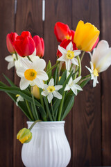 a bouquet of flowers made of tulips and daffodils in a vase on a wooden background. Floristics and botany