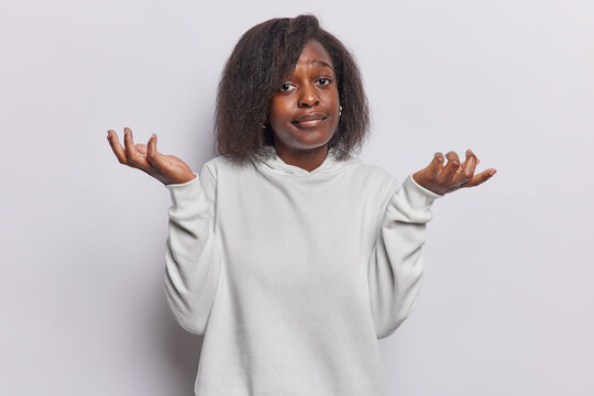 I dont know. Dark skinned woman shrugs shoulders spreads palms feels hesitant or unsure drssed in casual hoodie isolated on white background. Clueless Afro American female model faces Generative AI
