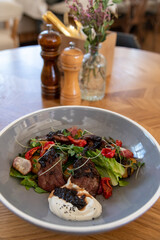 Close-up view of beef tagliata with cauliflower cream, wine sauce, small potatoes and cherry tomatoes on grey plate on wooden table in restaurant. Soft focus. Italian food theme.