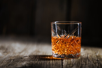 A glass of Whiskey on a rustic wooden board, that can be surface of barrel. Moody atmosphere.