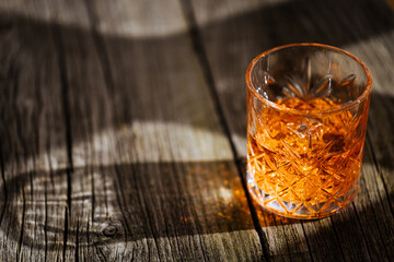 A glass of Whiskey on a rustic wooden board, that can be surface of barrel. Moody atmosphere.