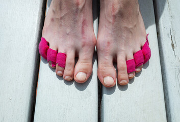 Brightly bandaged toes of a tired legs. Woman with removed shoes sitting on wooden bench, taking a break after a long day of hiking. 