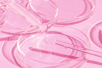 Dropping gel from a pipette into a Petri dish on a pink background. Cosmetics Lab. Serum, gel, retinol, oil.