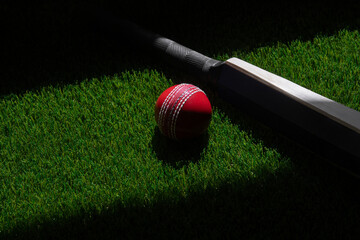 Cricket bat and red ball with natural lighting on green grass. Horizontal sport theme poster,...