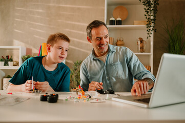 Happy father and his son sitting at the table and looking at the laptop.