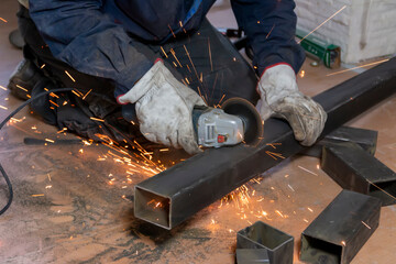 The hands of the master saw the metal bars with a grinder. Metal works. Close up