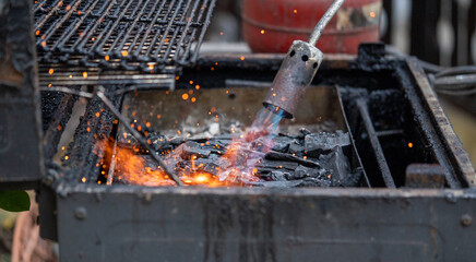 Man lighting up a grill with a gas fire blower torch
