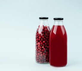 Bottle with berry juice from forest cranberries and lingonberries on a blue isolated background. Healthy drink concept.