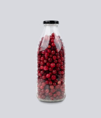 Bottle with wild cranberries and lingonberries on a gray isolated background. Healthy drink concept.