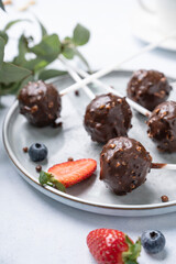 Chocolate cake pops with nuts on a plate with fresh berries on a light background close up. Homemade healthy candies on a stick.