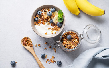 Homemade baked granola with yogurt, blueberries and banana in a bowl on a light background with fresh berries. Healthy vegetarian breakfast with muesli.