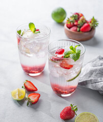 Fresh strawberry mojito in a glass with berries, lime, mint and ice on a light background with shadow. The concept of a summer refreshing drink for a party