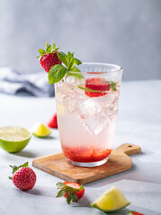 Fresh strawberry mojito in a glass with berries, lime, mint and ice on a light background with shadow close up. The concept of a summer refreshing drink. Front view